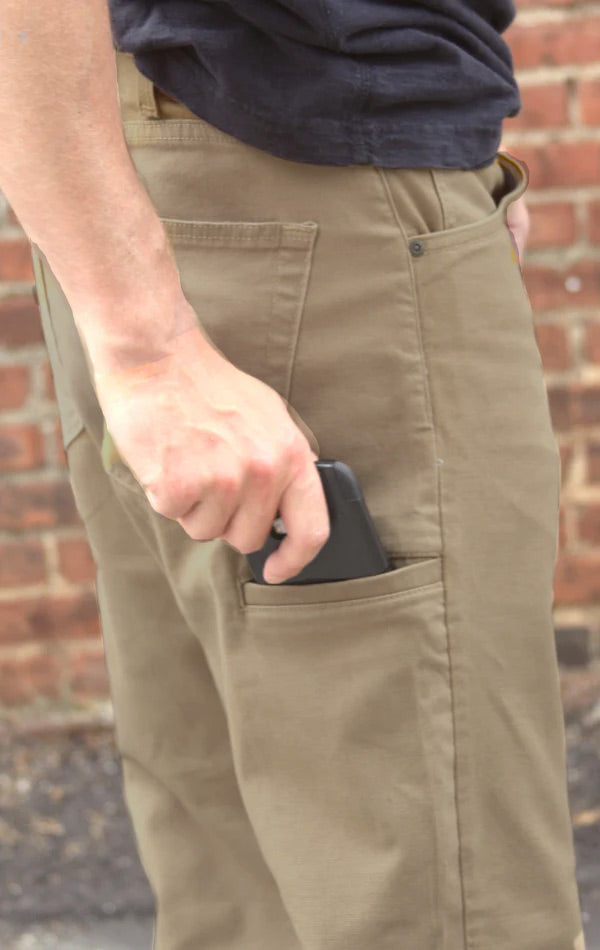 Person wearing brown pants with a phone in the pocket against a brick wall.